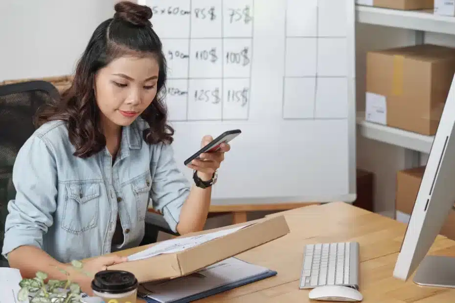 Imagem de uma mulher em seu home office com computador, celular, quadro branco e papéis em caixas aprendendo como ser mais organizada