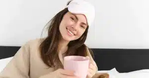 imagem de uma mulher sentada na cama com caneca para iniciar a rotina matinal de tim ferriss de produtividade
